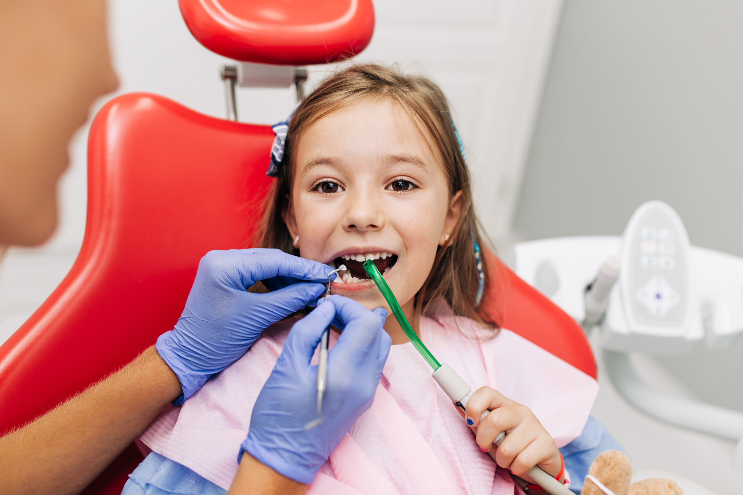 Cute little girl sitting on dental chair and having dental treatment.